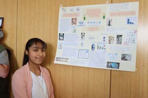 female student smiling and standing to side of poster