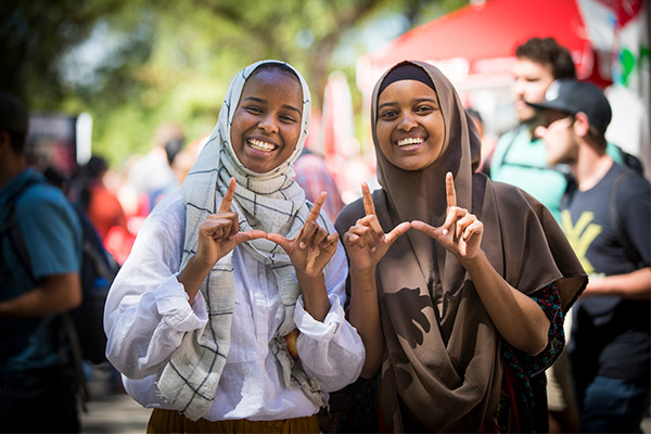 two students of color wearing Hijabs holding the block U handsign