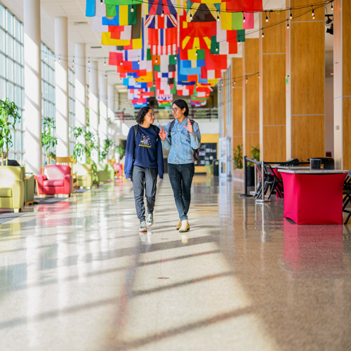 Two students of color walking down hallway of olpin union building decorated with flags overhead.