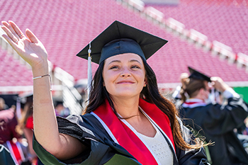 student in graduation attire smiling with university diploma